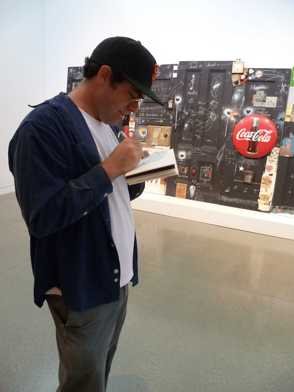A person seated in a museum gallery sketching in front of artworks, part of Adam Rozan's Art on Art initiative at the Oakland Museum of California.
