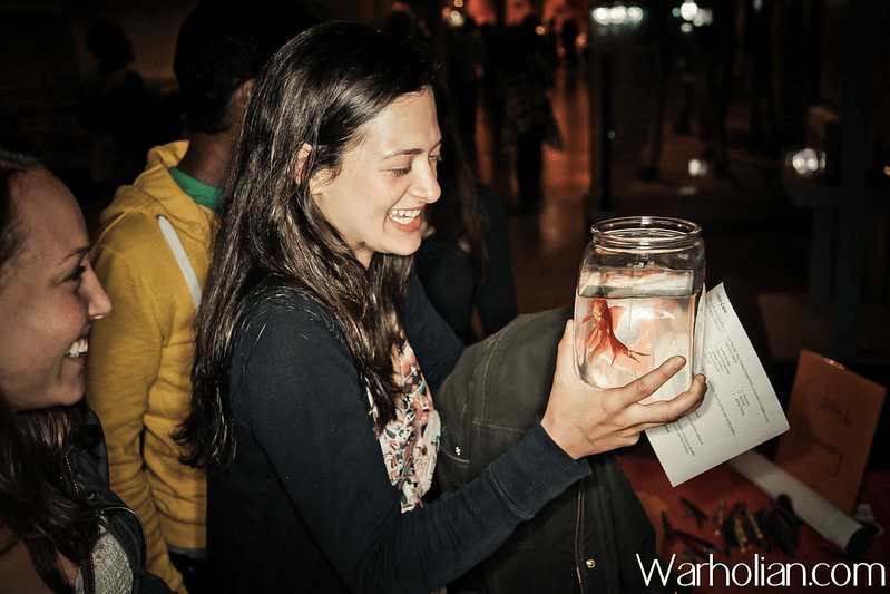 A visitor holding a jar containing a live goldfish at the Carassius Auratus Auratus Goldfish Society interpretation table, presented at the California Academy of Sciences.